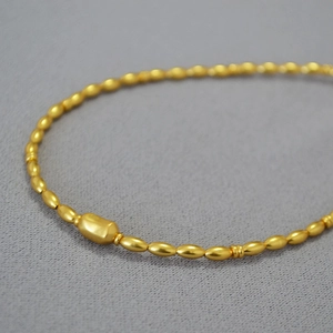 Macro shot of matte gold brass rice bead chain necklace with a central rectangle bead
