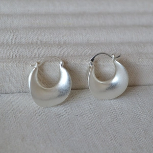 Detail of matte silver geometric curved earrings on textured beige fabric background