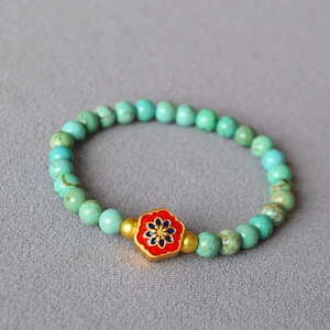 Macro shot of turquoise beads with red enamel flower and golden spacers on a textured surface