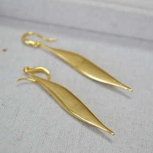 Detail of long gold leaf earrings with zircon accents on a textured fabric surface