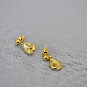 Macro view of polished gold teardrop earrings on grey textured fabric background