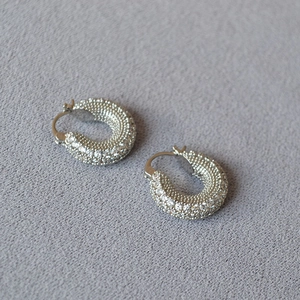 Close-up of thick silver hoop earrings paved with sparkling cubic zirconia on grey fabric