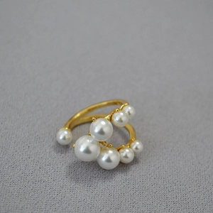 Macro di un anello in ottone placcato oro con perle bianche su sfondo grigio testurizzato