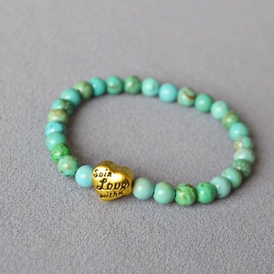 Macro detail of turquoise beaded bracelet featuring a gold heart pendant with romantic engraving