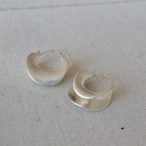 Macro detail of silver geometric earrings with irregular curved matte brushed texture