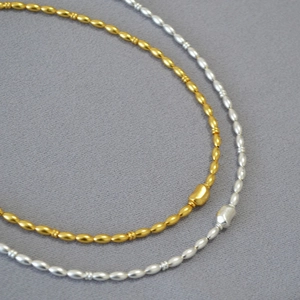 Detailed view of gold and silver beaded necklaces with irregular bean charms on grey fabric