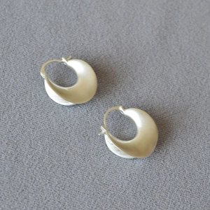 Detail of matte silver irregular geometric earrings on a textured gray fabric background