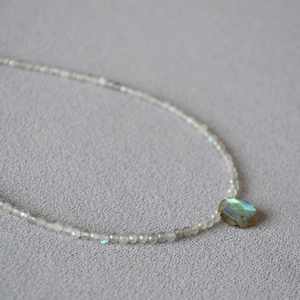 Macro detail of natural labradorite pendant with blue fire and grey beaded necklace chain