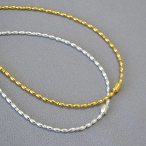 Detail of matte gold and silver olive bead necklaces on grey fabric background