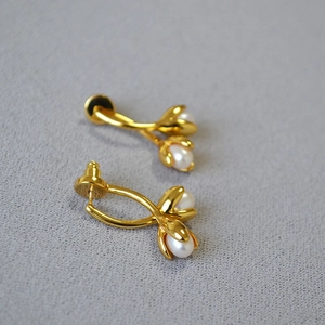 Detail of elegant gold tulip earrings featuring white pearls on grey fabric