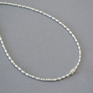 Detail of silver beaded necklace with oval rice beads and a central hexagonal metal bead