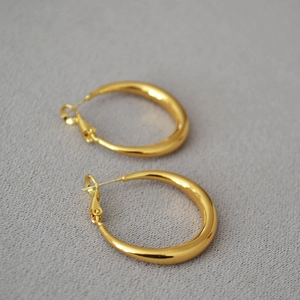 Detail of high-polish gold teardrop hoop earrings on a textured grey fabric background