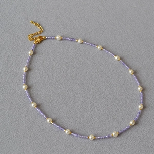 Detailed shot of handmade necklace with light purple stones, white pearls and gold clasp