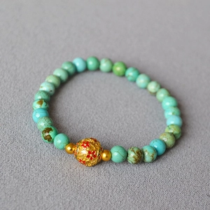Detail of vintage turquoise beaded bracelet featuring a gold floral enamel brass charm