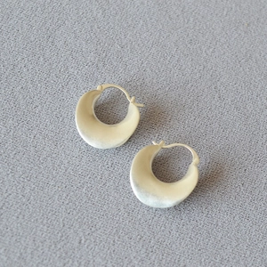 Detail of matte silver French retro double-layer geometric curved earrings on grey fabric
