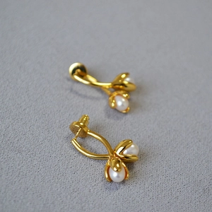 Elegant gold flower bud earrings with freshwater pearls on a grey textured background