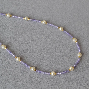 Elegant purple zircon and pearl necklace with gold spacers on grey textured fabric