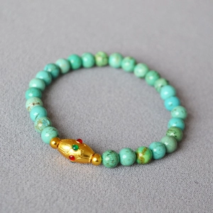 Detail of turquoise beaded bracelet featuring a gold-toned brass enamel spindle bead