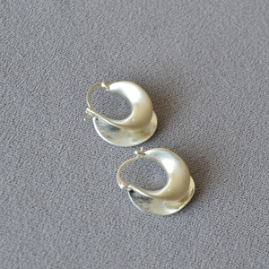 Macro shot of silver-colored matte wide C-shape earrings with smooth irregular geometry