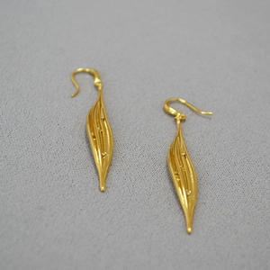 Macro detail of golden leaf drop earrings with sparkling zircon stones on grey fabric
