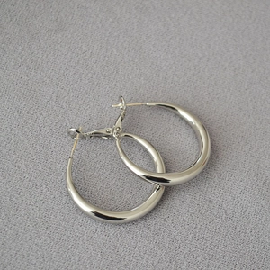 Detailed close-up of polished thick silver hoop earrings on a textured gray background