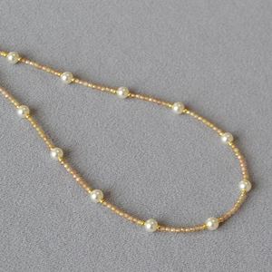 Macro shot of amber faceted beads and white pearls with golden spacers on a textured fabric