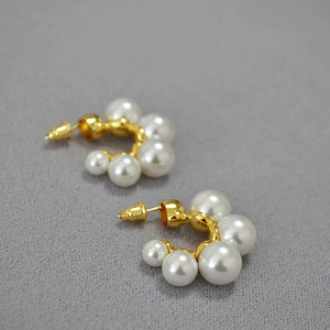 Detail view of C-shaped gold-plated brass earrings with tiered white imitation pearls