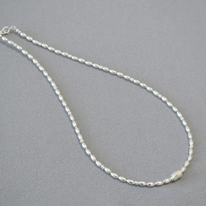 Detail of silver beaded necklace with smooth oval beads and central cylinder charm