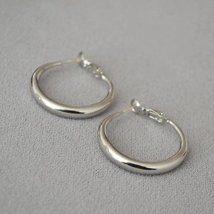 Close-up of polished thick silver hoop earrings on a grey textured fabric background