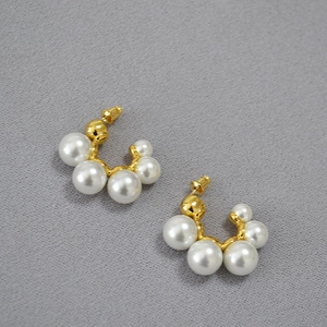 Detailed view of gold C-shape earrings featuring gradient white pearls on gray fabric