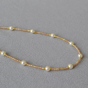 Sparkling yellow zircon and white pearl necklace with gold spacers on grey fabric