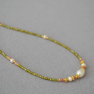 Détail macro de perles facettées vertes et de perles d'eau douce sur un collier d'or délicat