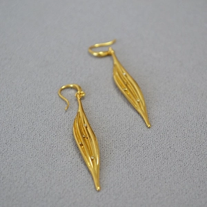 Detail of long gold leaf earrings with zircons and textured finish on gray fabric