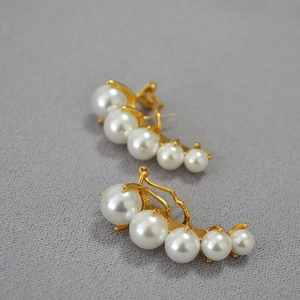 Close-up of gold curved earrings with five white gradient pearls on a textured background