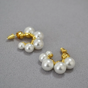 Detail of C-shaped gold-plated brass earrings with gradient pearls on dark grey background