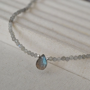 Macro shot of faceted labradorite beads with a blue flash teardrop pendant on beige fabric