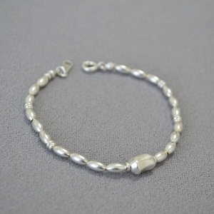 Macro shot of polished silver beaded bracelet with an irregular geometric centerpiece