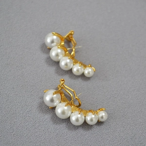 Macro shot of curved gold drop earrings with a row of five white gradient pearls