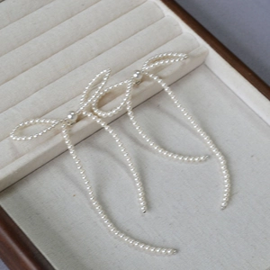 Elegant white pearl bow earrings with long tassels on a velvet jewelry tray