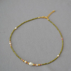 Gros plan d'un collier de perles d'eau douce et zircon vert sur fond en feutre gris