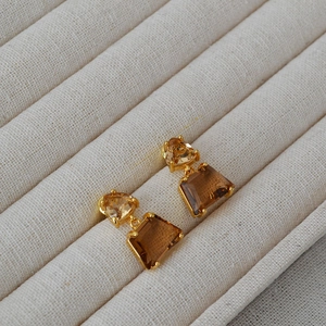 Detail of amber geometric earrings with gold trim on beige fabric display tray