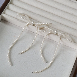 Detailed view of woven pearl bow earrings with long tassels on a beige display tray