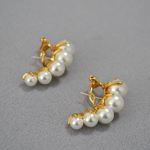 Detail of elegant gold curved pearl earrings with five white pearls on grey fabric