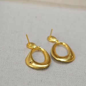 Detailed close-up of matte gold irregular oval earrings on a canvas background