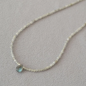 Macro view of dainty grey bead necklace featuring a blue teardrop labradorite pendant