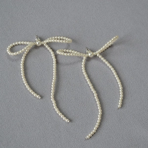 Detail of handmade bow-shaped earrings with long imitation pearl tassels on fabric