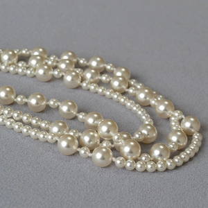 Macro detail of multi-layered faux pearl necklace with high-gloss finish on grey fabric