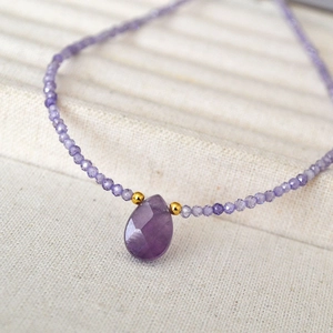 Close-up of faceted purple amethyst teardrop pendant with gold beads on a beaded chain