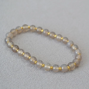 Detail of grey agate beaded bracelet with gold spacers on a textured fabric