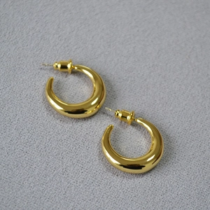 Detailed close-up of polished gold-plated crescent hoop earrings on a grey textured fabric